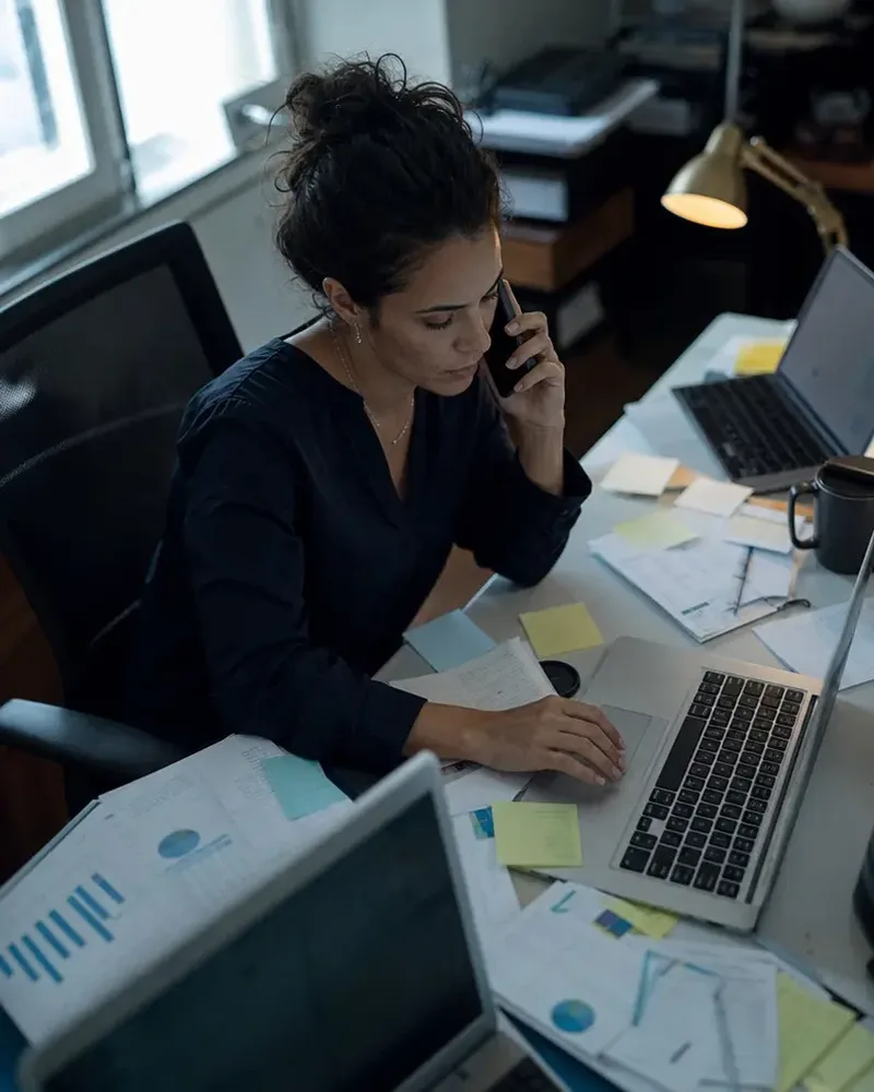 Profissional soterrada em notebooks, relatórios e ligações, resolvendo tudo ao mesmo tempo